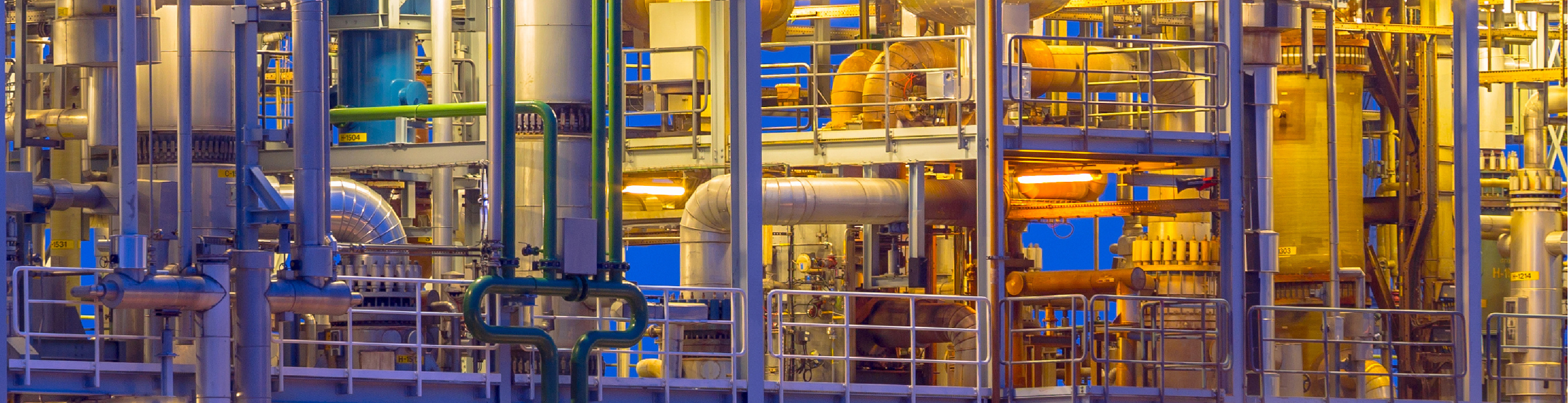 Hero image of a colorfully lit industiral site showing lots of insulated pipes and vessels