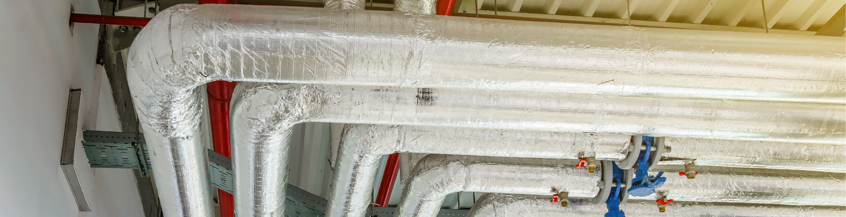Hero image of large pipes suspended form the ceiling wraped in silver insulation