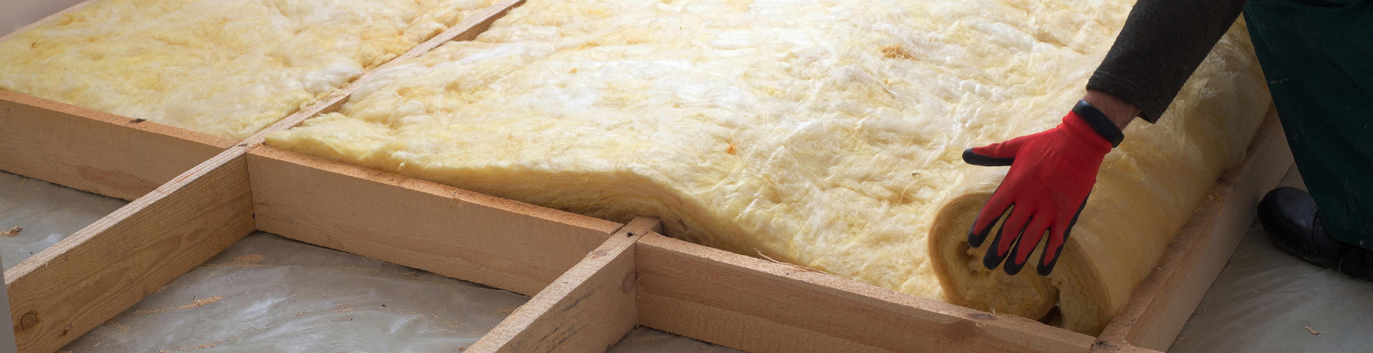 Hero photo showing a workman laying rolls of residential insulation in a attic or floor space